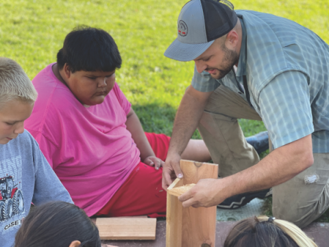 A mission volunteer from F5 Challenge builds a birdhouse with students.