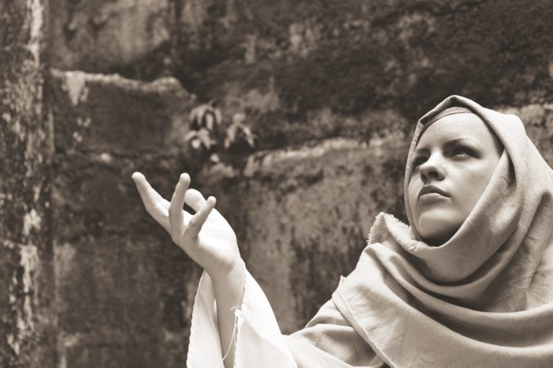 A woman dressed in Biblical clothing raising her hand as if in prayer or to beg. Could be the Virgin Mary.