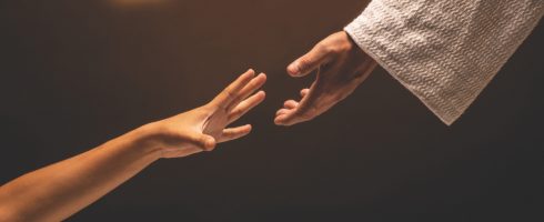 Jesus Christ reaching out to help those in need in a room lit with warm lights.
