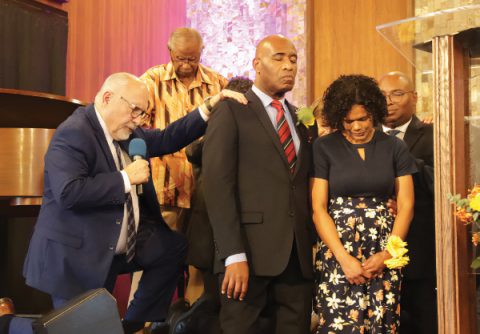 Ordained pastors lay hands on Baptiste and his wife as Cress offers the ordination prayer.