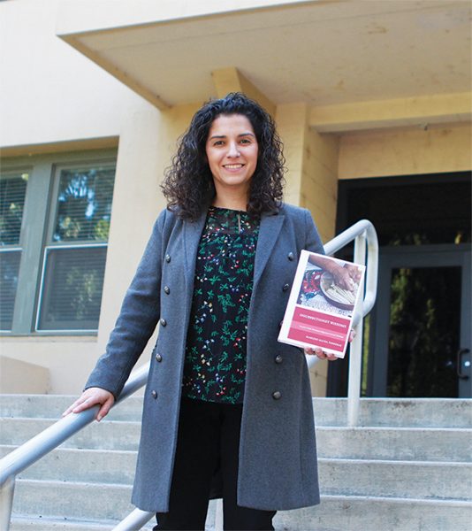 Dr. Marlene Ferreras poses with a copy of her book on the steps of La Sierra Hall, which houses the H.M.S. Richards Divinity School where she teaches.