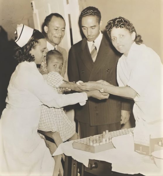 Dr. Temple administers vaccine. Looking on
is Dr. Owen A. Troy (left), president of the Community Health Association.<br /><em>Photo courtesy of Dr. Carmelita Troy</em>.