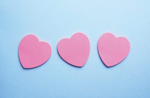 Pink heart shaped sticky notes organized in a row over blue background, top view