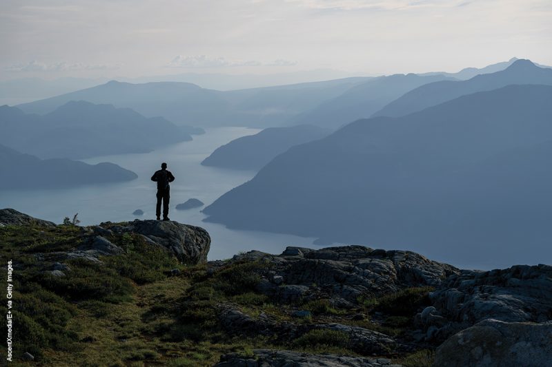 Hiker pauses on mountain ridge above coastal mountains and inlet