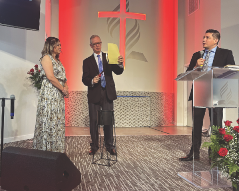 Liz Barraza (izquierda) observa a Reggie Leach quemar una copia de la hipoteca de Phoenix Central Valley Spanish mientras el pastor Adino Salazar (derecha) dirige a la congregación en una lectura de compromiso como parte de la ceremonia.