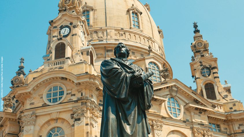 Monument of Martin Luther - the founder of the Reformation. The man holds a book in his hands and looks away, dressed in a gown.