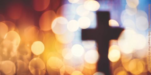 Abstract defocussed cross silhouette in church interior against stained glass window concept for religion and prayer
