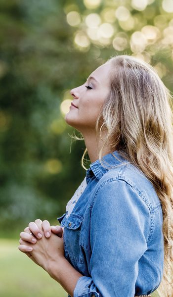 A woman in a blue dress praying in the garden under the sunlight with a blurry background