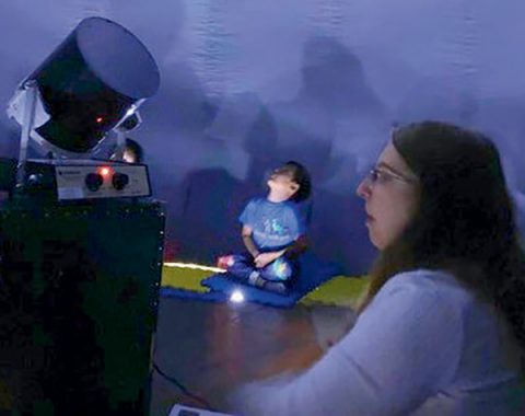 Chandra Young (right) controls the equipment that projects the solar system on the interior of the STARLAB as students look up into the “heavens.”