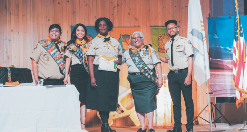 <p>Patsy receives her certificate of achievement and badges, celebrating her accomplishments in honors like Camping Beginner, Camping Advanced, and Archery.</p><p>Patsy recibe su certificado de logro e insignias, celebrando sus logros en honores como Principiante en Camping, Campamento Avanzado y Tiro con Arco.</p>