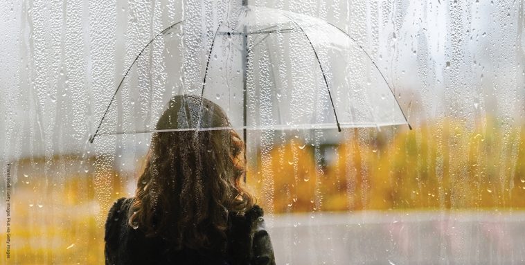 A woman silhouette with transparent umbrella through wet window with drops of rain. Autumn