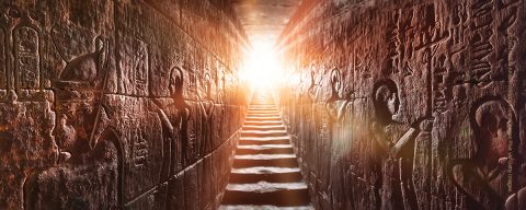 Egypt Edfu temple, Aswan. Passage flanked by two glowing walls full of Egyptian hieroglyphs, illuminated by a warm orange backlight from a door