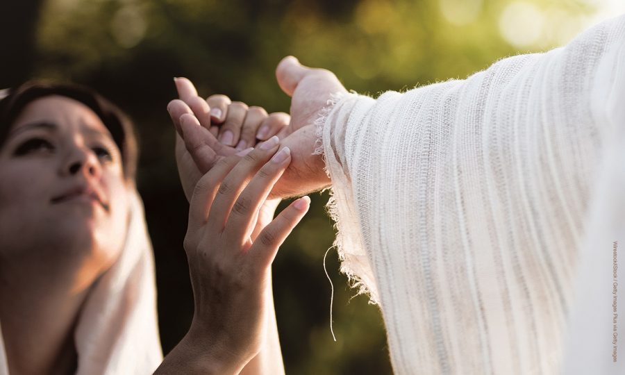 A shallow focus shot of a female grabbing the hand of Jesus Christ for healing and help
