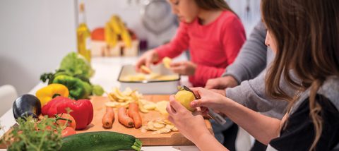 Close-up photo of two little girls cooking in the kitchen together with their father