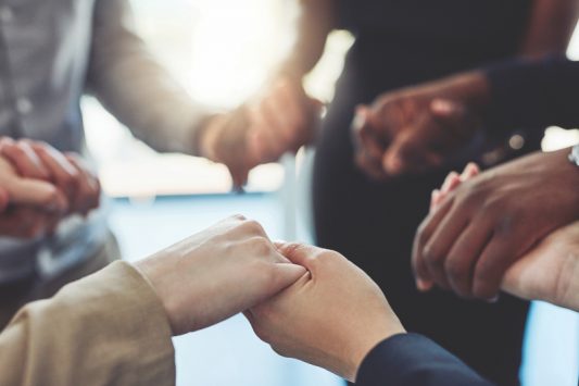 Cropped shot of a group of businesspeople standing together and holding hands in a modern office