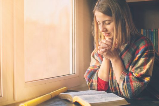 Beautiful woman praying having the Bible opened in front of he