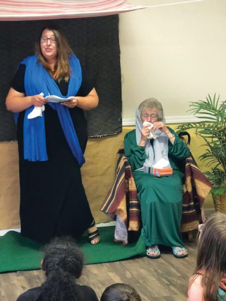 Karen Schneider, NUC treasurer, portraying Mary Magdalene, relates the story of the crucifixion to the children at the Sparks VBS as her mother, Ardith Schneider, conveys the emotion of the story.