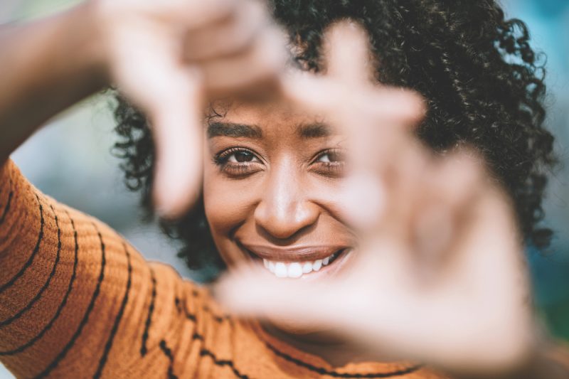 A beautiful African American woman smiles while framing her face with her fingers.  Shot in Los Angeles, California.