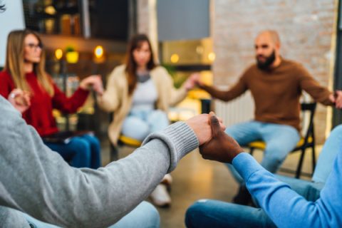 Group of young people holding hands and sitting all together on group therapy in circle