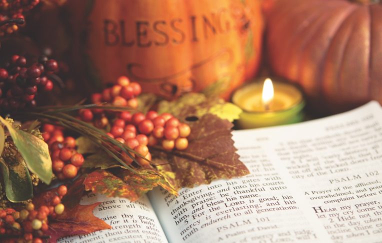 Open Bible showing Scripture Psalms 100:4 with autumn colored berries, leaves and candle. There are two pumpkins in background, one pumpkin is inscribed with "blessings". Focus on verse 4. Horizontal image would be good for Christian or religious Thanksgiving. 
