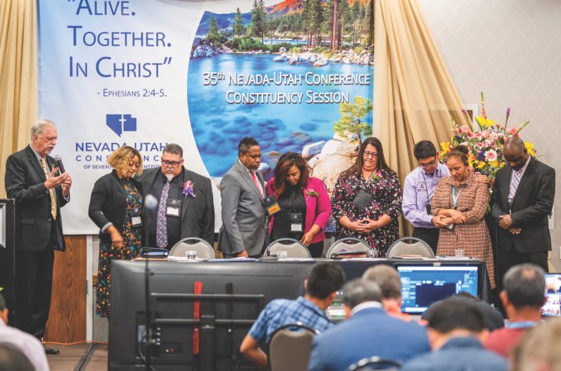 Pacific Union Conference President Bradford Newton offers a prayer of consecration to new officers and their spouses. Samantha Camacho, Carlos Camacho, Keith Henry, Chanda Nunes-Henry, Karen Schneider, Benjamin Carballo, Veronica Carballo, and Oneil Madden.