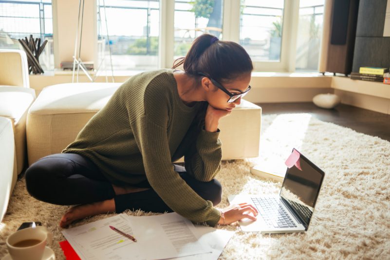 young woman studying and working on her laptop,sitting on the carpet in the living room,nice sunny day