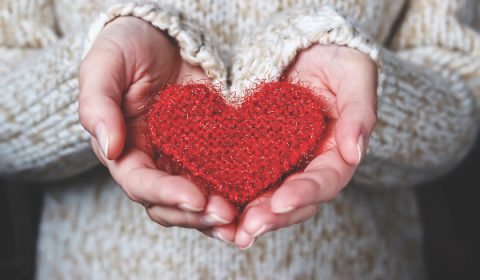 Girl in a light sweater gives a knitted heart. Close-up