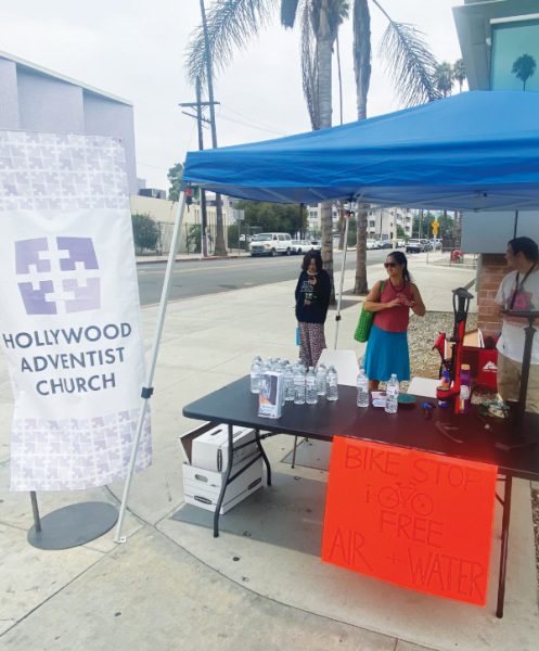 Los voluntarios de pie junto a su anuncio de agua y aire gratis. El edificio de la iglesia de Hollywood no tenía los cuatro pies requeridos de espacio en la acera, por lo que la carpa se instaló frente a la estación de bomberos en la esquina opuesta a la iglesia.