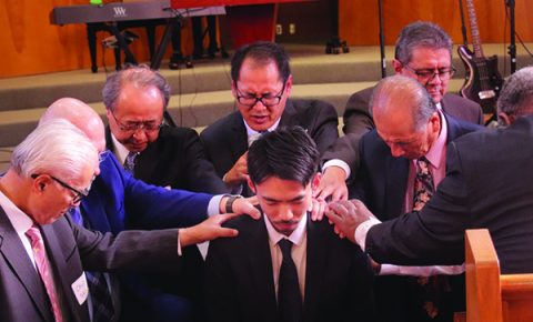Ordained pastors lay hands on Shinasue during the ordination prayer.