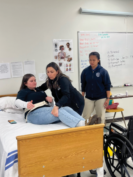 La instructora de CNA Eva González demuestra la forma correcta de transferir a un paciente de una cama a una silla de ruedas.